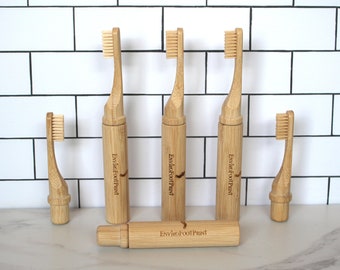 May include: Five bamboo toothbrushes with the text "EnviroFootPrint" engraved on the handle. The toothbrushes are arranged in a row on a white tiled surface.