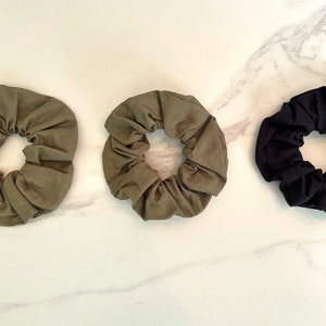May include: Three fabric scrunchies in green, olive green, and black. The scrunchies are made of soft, stretchy fabric and are perfect for holding hair in place.