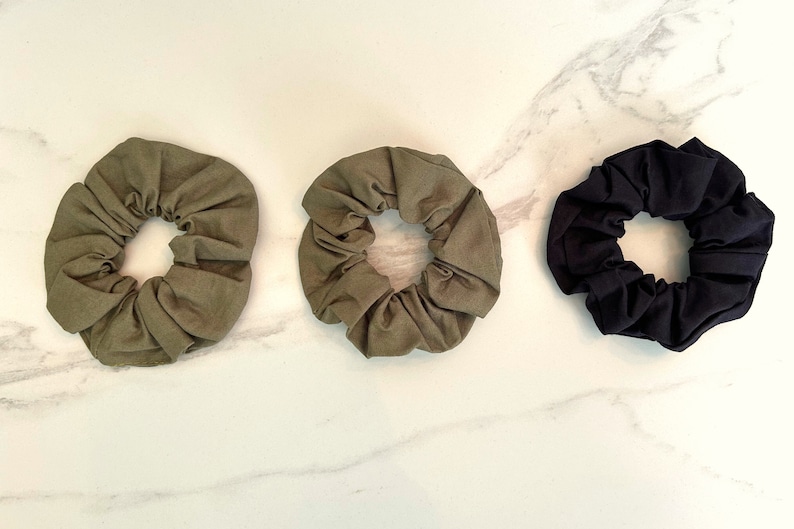 May include: Three fabric scrunchies in green, olive green, and black. The scrunchies are made of soft, stretchy fabric and are perfect for holding hair in place.