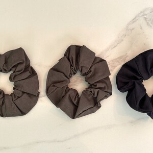 May include: Three fabric scrunchies in different colors: dark gray, light gray, and black. The scrunchies are made of soft, stretchy fabric and are perfect for holding hair in place.