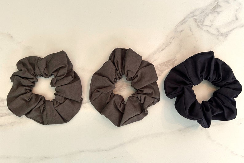 May include: Three fabric scrunchies in different colors: dark gray, light gray, and black. The scrunchies are made of soft, stretchy fabric and are perfect for holding hair in place.