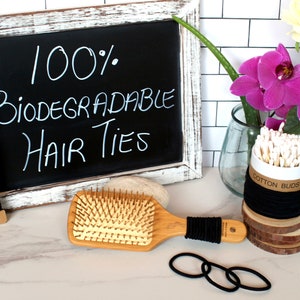 May include: A set of black hair ties, a wooden hair brush, a container of cotton buds, and a chalkboard sign that reads "100% Biodegradable Hair Ties".