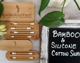 May include: Bamboo and silicone cotton swabs in bamboo cases. The cases are rectangular with rounded edges and feature the text "EnviroFootPrint" and a footprint logo. The image also includes a chalkboard sign that reads "Bamboo & Silicone Cotton Swabs."