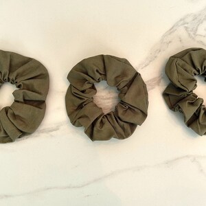 May include: Three olive green scrunchies made of fabric.