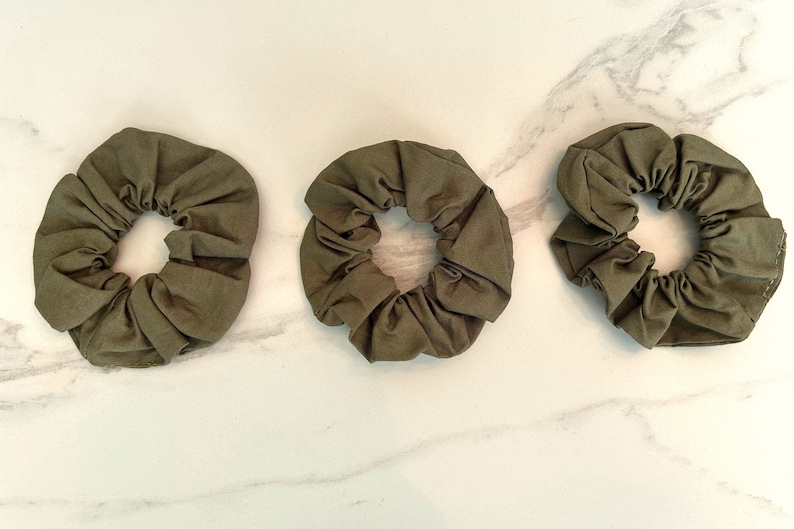 May include: Three olive green scrunchies made of fabric.
