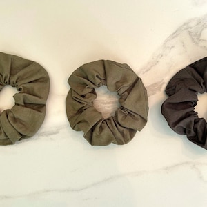 May include: Three fabric scrunchies, two in a dark olive green and one in black.