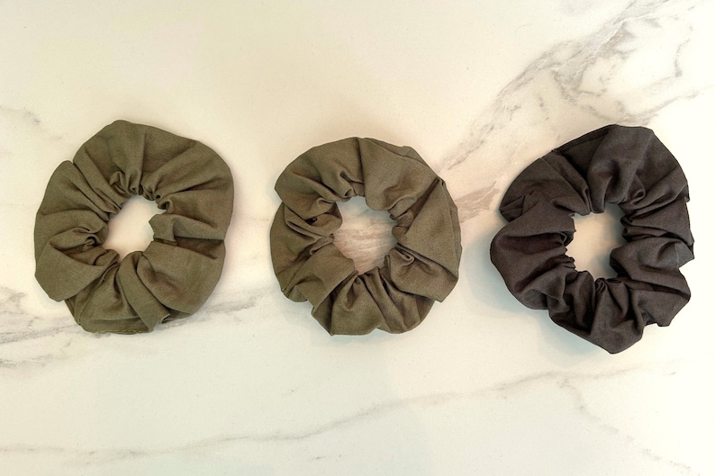 May include: Three fabric scrunchies, two in a dark olive green and one in black.