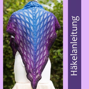 Puede incluir: Un chal de ganchillo morado, azul y negro con un patrón de encaje. El chal está drapeado sobre un maniquí blanco.