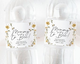 Op de afbeelding: Twee doorzichtige plastic waterflessen met etiketten waarop "Mommy to Bee!" staat met een bloemenmotief en bijen. De etiketten bevatten ook de tekst "Savannah's Baby Shower" en "June 4, 2022".