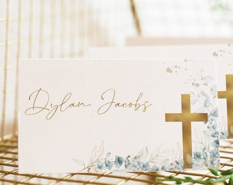 May include: Place cards with a watercolor floral design and gold cross accents. The cards are printed with the name "Dylan Jacobs".