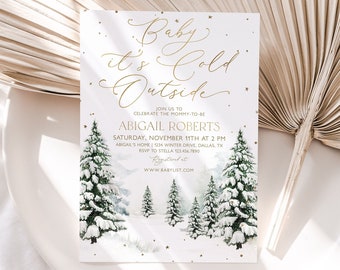 May include: A white baby shower invitation with gold lettering that reads "Baby it's cold outside". The invitation features a watercolor illustration of a snowy forest with pine trees and gold stars.