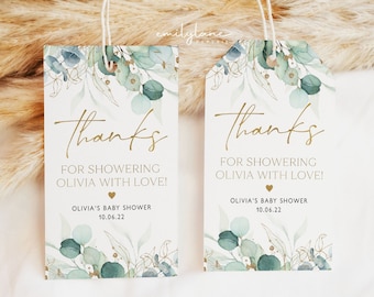 May include: Two white thank you tags with gold lettering and a watercolor design of green leaves. The text on the tags reads "Thanks for showering Olivia with love!" and "Olivia's Baby Shower 10.06.22".