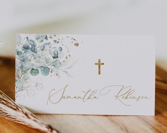 May include: White place card with a gold cross and the name "Samantha Robinson" written in gold script. The card has a watercolor design of eucalyptus leaves and gold accents.