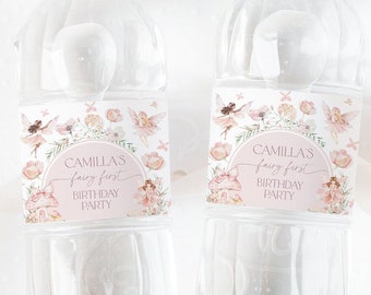 Peut inclure: Deux bouteilles d'eau en plastique transparent avec des étiquettes roses et blanches. Les étiquettes présentent un thème de fée avec le texte "Camilla's fairy first birthday party".