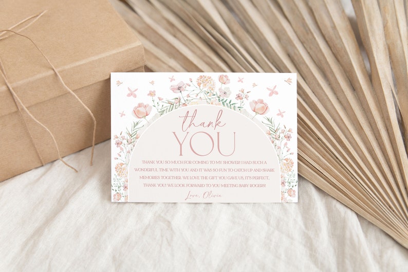May include: A thank you card with a floral design and the text "thank you" in a pink circle. The card has a pink and white floral border and the text "Thank you so much for coming to my shower. I had such a wonderful time with you and it was so fun to catch up and share memories together. We love the gift you gave us, it's perfect. Thank you! We look forward to you meeting baby Rogers. Love, Olivia."