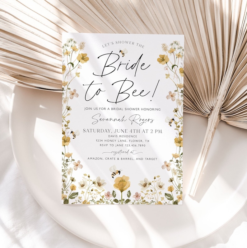 以下が含まれることがあります： 黄色と白の花柄のデザインと「Let's shower the Bride to Bee!」というテキストが書かれた、花柄のブライダルシャワー招待状。サバンナ・ロジャースを称えるブライダルシャワーにご参加ください。土曜日、6月4日午後2時。デイビス邸。1234 Honey Lane, Flower, TX。ジェーン 123.456.7890 まで RSVP をお願いします。Amazon、Crate & Barrel、Target で登録済みです。