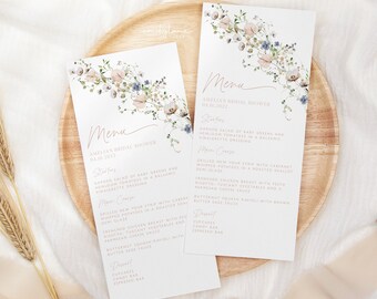 Puede incluir: Un menú para la despedida de soltera de Amelia con un diseño floral. El menú incluye aperitivos, plato principal, postre y bebidas. Los aperitivos son una ensalada de jardín de verduras tiernas y tomates antiguos en una vinagreta balsámica. El plato principal es un filete de Nueva York a la parrilla con patatas batidas con Cabernet en una salsa de chalota asada. El postre es cupcakes, una barra de dulces y una barra de espresso.