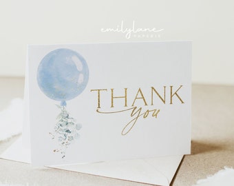 May include: A white thank you card with a blue watercolor balloon and gold lettering that says "THANK you". The balloon has a sprig of green leaves hanging from it.