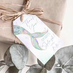 Puede incluir: Una etiqueta de agradecimiento con una ilustraci&oacute;n de cola de sirena. La etiqueta es blanca con un fondo degradado azul claro y verde. El texto en la etiqueta dice "&iexcl;Gracias! Por hacer de mi fiesta un Splash! Con amor, Bella."
