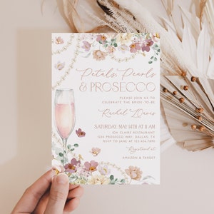 May include: A bridal shower invitation with a floral design and a glass of pink prosecco. The invitation reads "Petals, Pearls & Prosecco" and includes the bride-to-be's name, Rachel Davis, the date and time of the event, and the location. The invitation also includes the text "Registered at Amazon & Target".