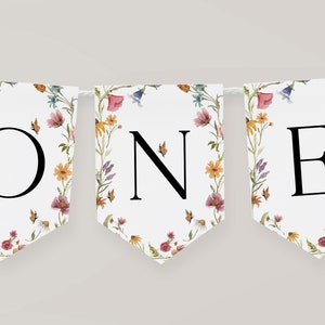 K&ouml;nnte beinhalten: Ein wei&szlig;es Banner mit einem Blumenmuster und dem Wort "ONE" in schwarzen Buchstaben. Das Banner ist perfekt f&uuml;r eine erste Geburtstagsfeier.