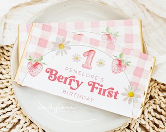 May include: A pink and white gingham patterned chocolate bar wrapper with a watercolor illustration of strawberries and daisies. The text on the wrapper reads "Berry First Birthday" with the number "1" and the name "Penelope's".