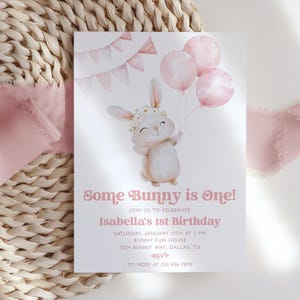 Op de afbeelding: Een roze en witte uitnodigingskaart met een aquarel-illustratie van een konijn dat roze ballonnen vasthoudt. De tekst luidt "Some Bunny is One!" en "Isabella's 1st Birthday".