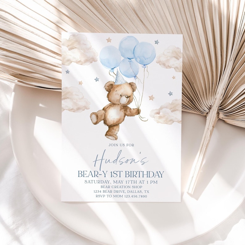 May include: A blue and white invitation with a watercolor illustration of a teddy bear holding blue balloons. The text reads "Join us for Hudson's Bear-Y 1st Birthday, Saturday, May 17th at 1 PM, Bear Creation Shop, 1234 Bear Drive, Dallas, TX, RSVP to Mom 123.456.7890".