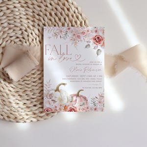 May include: Fall in love bridal shower invitation with a watercolor floral design featuring pumpkins, leaves, and roses in shades of pink and orange. The invitation text reads "Fall in love" with a heart and "Bridal Shower in honor of [Name]" with the date, time, and location.
