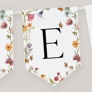 K&ouml;nnte beinhalten: Ein wei&szlig;es Banner mit einem floralen Rand und dem Buchstaben "E" in Schwarz. Die Blumen sind in den Farben Rosa, Gelb, Orange und Blau.