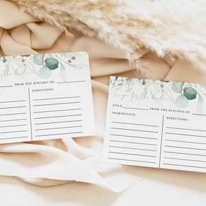 May include: Two white recipe cards with the text "Recipe for the Bride" in gold script. The cards have a watercolor eucalyptus and gold leaf design. Each card has spaces for title, ingredients, and directions.
