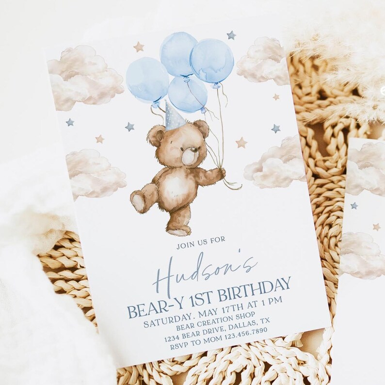 May include: A blue and white invitation for a first birthday party with a teddy bear holding balloons. The invitation says "Join us for Hudson's Bear-y 1st Birthday. Saturday, May 17th at 1 PM. Bear Creation Shop, 1234 Bear Drive, Dallas, TX. RSVP to Mom 123.456.7890"