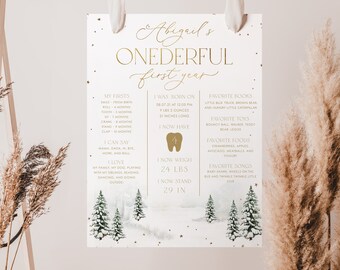 May include: A white printable poster with gold text and illustrations of snowy pine trees. The poster is a first birthday milestone chart for a baby named Abigail. It includes details like her birth date, weight, height, firsts, favorite foods, toys, books, and songs.