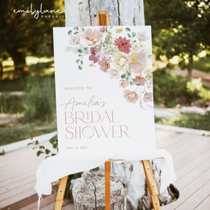 May include: A white welcome sign with pink floral illustrations and the text "Welcome to Amelia's Bridal Shower May 14, 2022".
