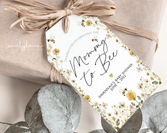 May include: A white tag with a floral design and the text "Mommy to Bee" and "Savannah's Baby Shower June 4, 2022".