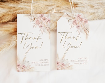 May include: Two white thank you tags with gold lettering and a watercolor floral design. The text on the tags reads "Thank You!" and includes the event details: Amelia's Bridal Shower, April 12, 2022.