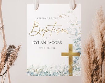 May include: A white sign with gold lettering announcing a baptism for Dylan Jacobs on March 12, 2022. The sign is decorated with watercolor blue and green leaves and a gold cross.