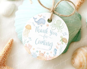 May include: A round gift tag with a nautical theme. The tag features a blue whale, octopus, jellyfish, and other sea creatures. The text "Thank you for Coming" is written in a script font. The tag is tied with twine and rests on a seashell.