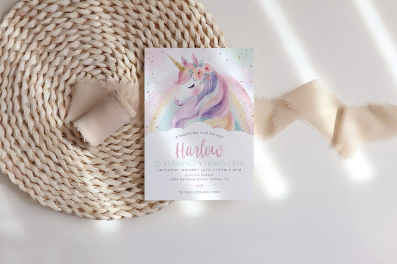 May include: A pastel-colored invitation card featuring a watercolor unicorn with a rainbow mane and floral crown. The card reads "Harlow is turning 4 years old!" and includes event details. The card is set on a woven placemat with a ribbon.