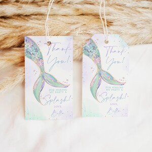 Puede incluir: Dos etiquetas de agradecimiento en forma de cola de sirena con un dise&ntilde;o de acuarela p&uacute;rpura y verde. El texto dice "&iexcl;Gracias!" y "Por hacer de mi fiesta un Splash! Con cari&ntilde;o, Bella".