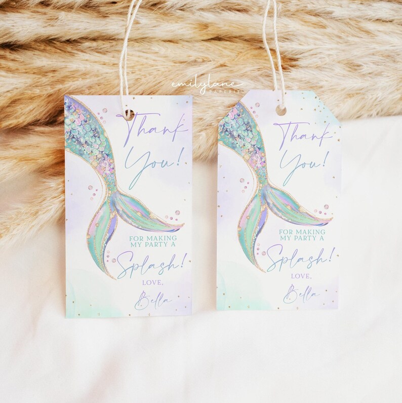 Puede incluir: Dos etiquetas de agradecimiento en forma de cola de sirena con un fondo de acuarela en tonos de morado, verde y azul. Las etiquetas presentan detalles de purpurina dorada y el texto "&iexcl;Gracias!" y "Por hacer de mi fiesta un Splash! Con cari&ntilde;o, Bella".