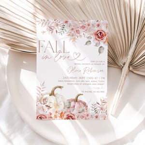 May include: Fall in love bridal shower invitation with a watercolor design featuring pumpkins, flowers, and leaves in shades of pink, white, and green. The text "Fall in love" is written in a script font with a heart symbol. The invitation includes the bride's name, the date and time of the shower, the location, and the registry information.