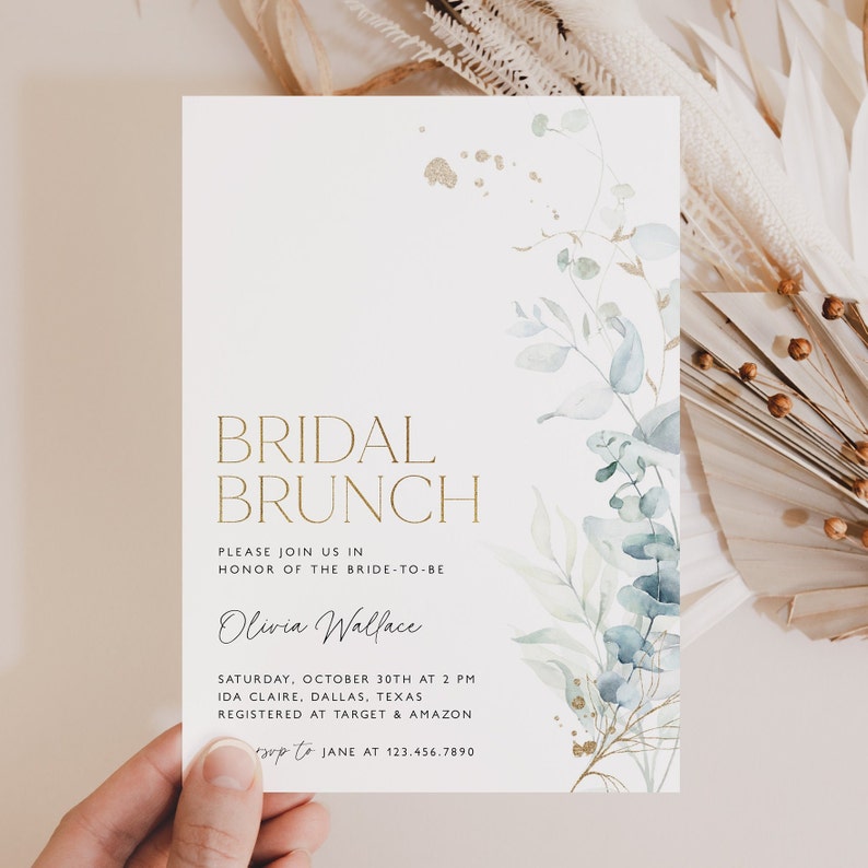 May include: A white invitation card with gold lettering announcing a bridal brunch for Olivia Wallace. The card features a watercolor illustration of eucalyptus leaves and gold accents.