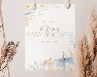 Puede incluir: Un cartel blanco con letras doradas que anuncia "Bienvenido al Baby Shower de Robyn" con la fecha "30 de octubre de 2022". El cartel está decorado con ilustraciones de calabazas y hojas en acuarela.