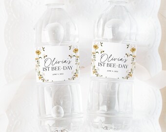 May include: Two clear plastic water bottles with white labels. The labels have a floral design with bees and the text "Olivia's 1st Bee-Day June 4, 2022".
