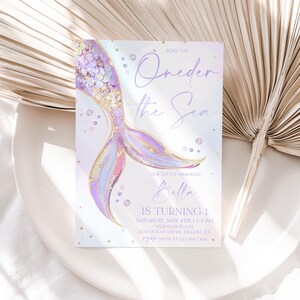 May include: A purple and gold mermaid tail illustration with glitter and iridescent accents. The invitation reads "Oneder the Sea" and includes the name "Bella" and details for a first birthday party.