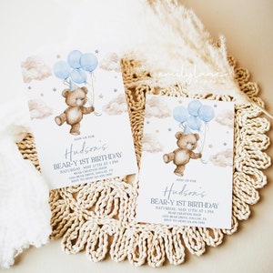 May include: Blue and brown teddy bear holding blue balloons with a party hat on its head. The bear is flying in the clouds with stars. The invitation says "Join us for Hudson's Bear-Y 1st Birthday. Saturday, May 17th at 1 PM. Bear Creation Shop. 1234 Bear Drive, Dallas, TX. RSVP to Mom 123.456.7890"