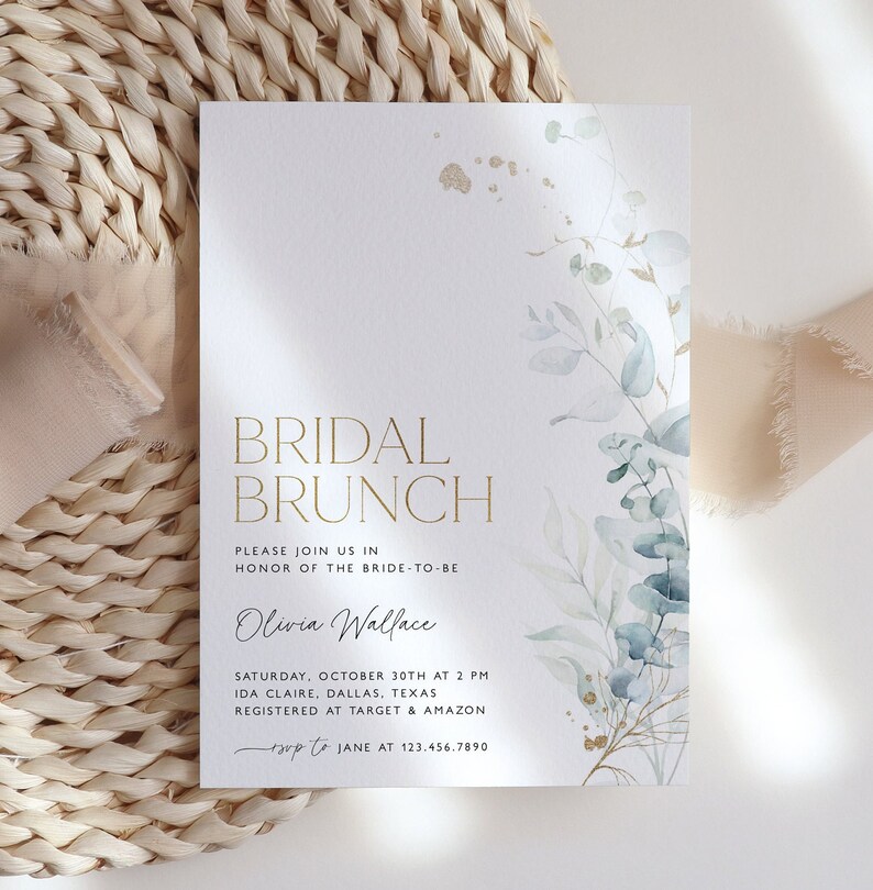 May include: A white invitation card with gold lettering for a bridal brunch. The card features a watercolor illustration of eucalyptus leaves and gold accents. The text reads "Bridal Brunch", "Please join us in honor of the bride-to-be Olivia Wallace", "Saturday, October 30th at 2 PM", "Ida Claire, Dallas, Texas", "Registered at Target & Amazon", "RSVP to Jane at 123.456.7890".