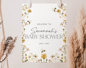 May include: A white baby shower sign with a floral border and bees. The sign says "Welcome to Savannah's Baby Shower" and "June 4, 2022".