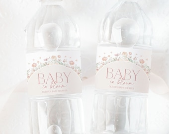 Könnte beinhalten: Zwei durchsichtige Plastikwasserflaschen mit Etiketten, auf denen "Baby in Bloom" und "Olivia's Baby Shower" steht. Die Etiketten haben ein florales Design mit rosa und pfirsichfarbenen Blumen.
